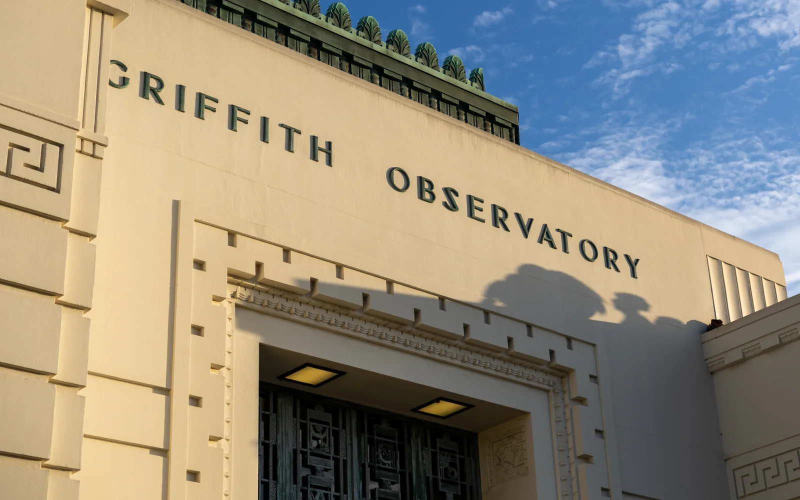 The Art Deco facade of Griffith Observatory, lettered GRIFFITH OBSERVATORY, against a blue sky